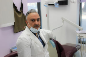 A man in white lab coat and mask sitting on chair.