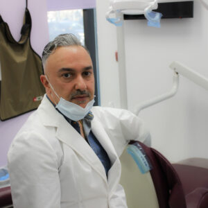 A man in white lab coat and mask sitting on chair.