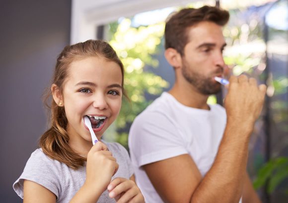 A girl and man brushing their teeth together.