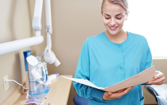 A woman in blue scrubs holding papers and smiling.